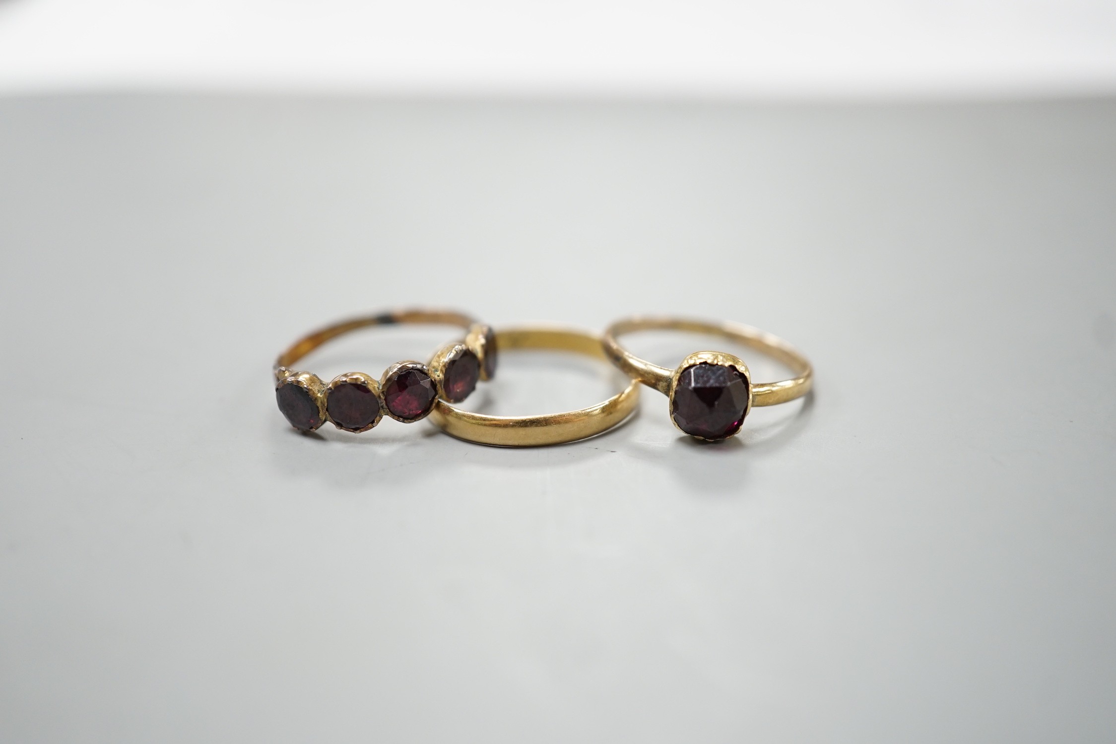 Two 19th century yellow metal and garnet set rings, including five stone half hoop, size J and single stone, size G/H and a yellow metal posy ring inscribed 'Vertue Gaineth Glory', gross weight 2.9 grams.